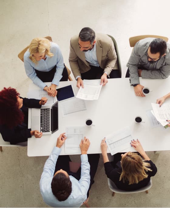 Overhead shot of workers sitting around a conference table reviewing paperwork and creative material