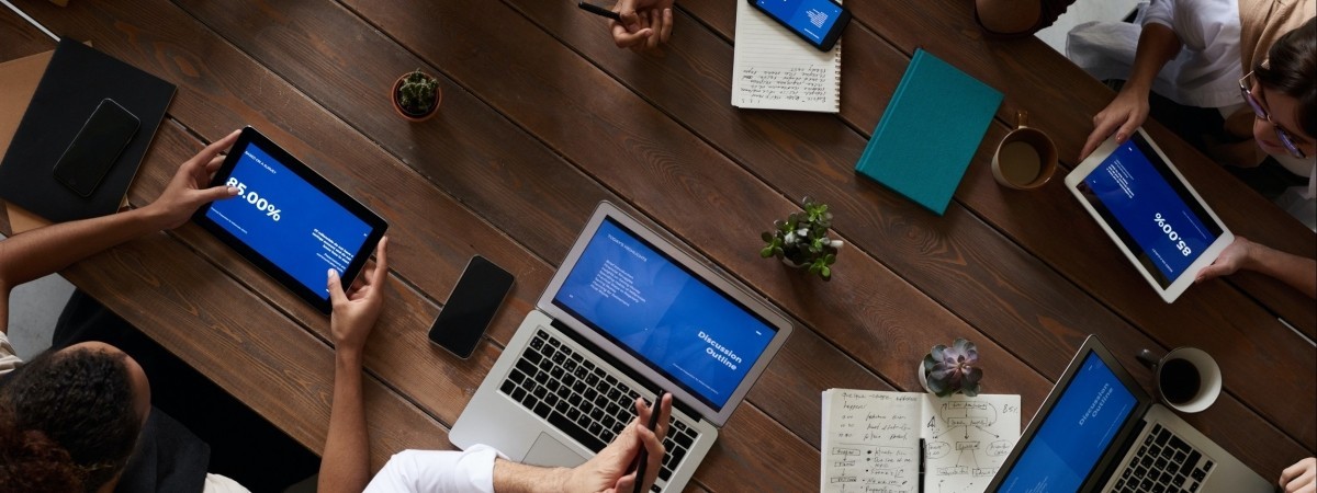 About Easy Savings: In New York, New York Colleagues gathered at table for a business meeting. On the table there are 2 cups, 3 notebooks, 3 succulents, 2 laptops, 2 tablets and a smartphone.