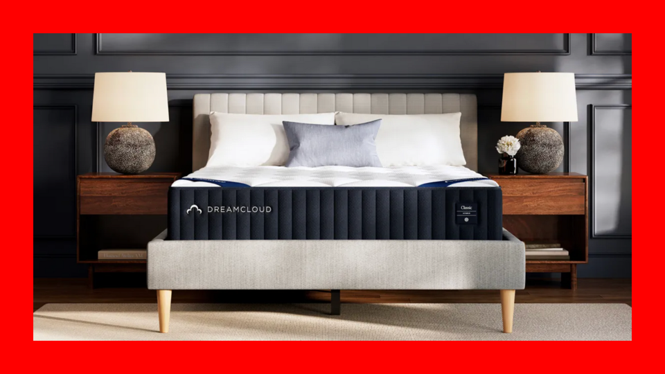 A DreamCloud mattress on an upholstered bed frame next to two bedside tables and lamps