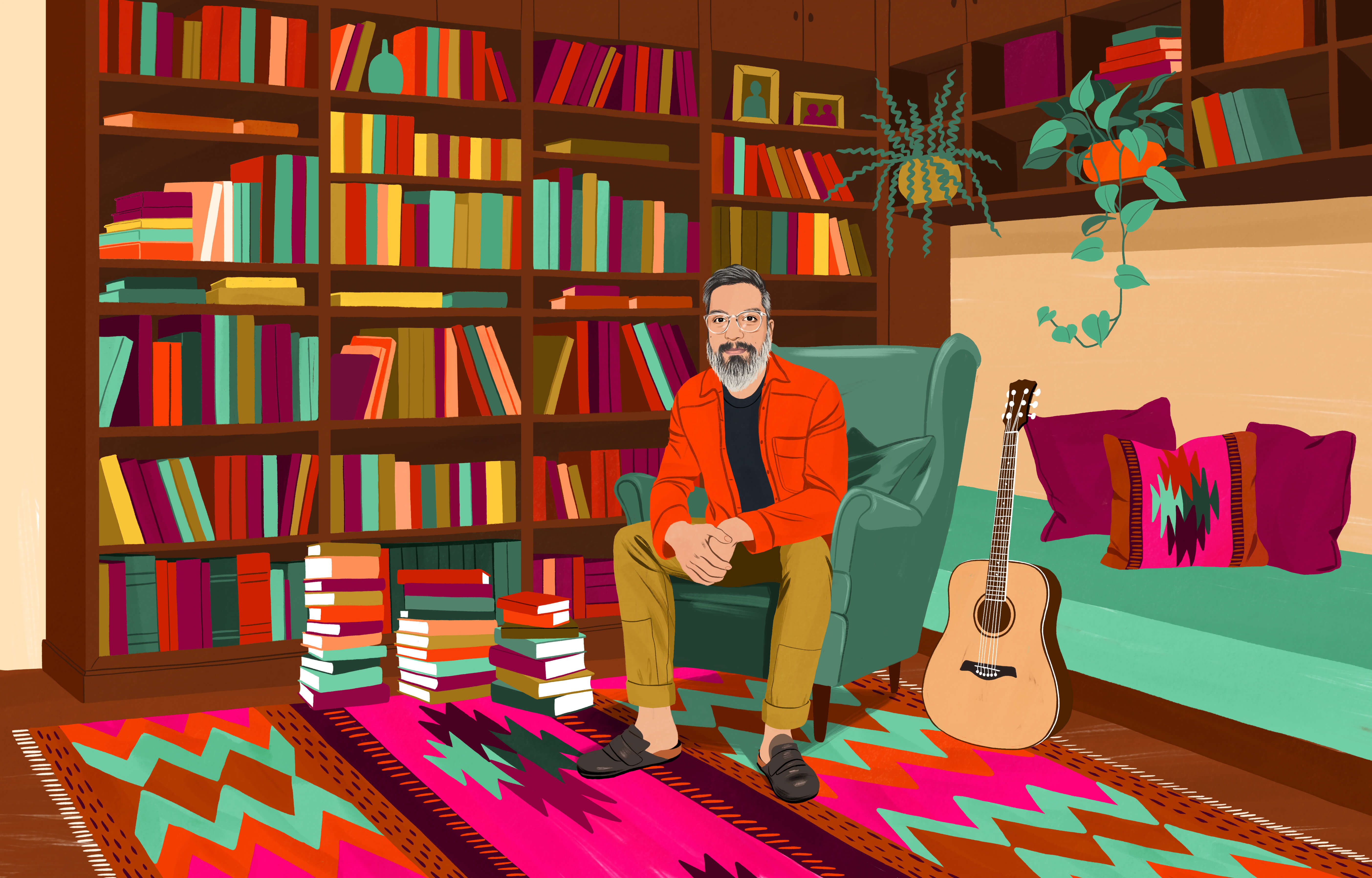 JP sitting in a wingback chair surrounded by many books in bookcases and stacked high on the floor. On the floor is a traditional Chilean rug with a colorful pattern. An acoustic guitar is within armโs reach.