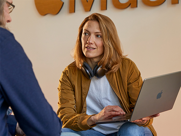 Zwei Apple Sales und Business Development Teammitglieder im Gespräch, eine Person hält ein MacBook und sitzt vor einer Wand mit dem Apple Music Logo darauf.