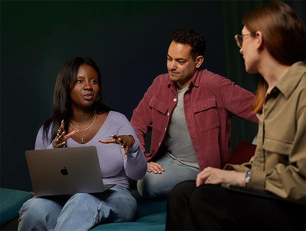 Drei Apple Software und Services Teammitglieder unterhalten sich auf einer Couch, eine Person mit einem MacBook.