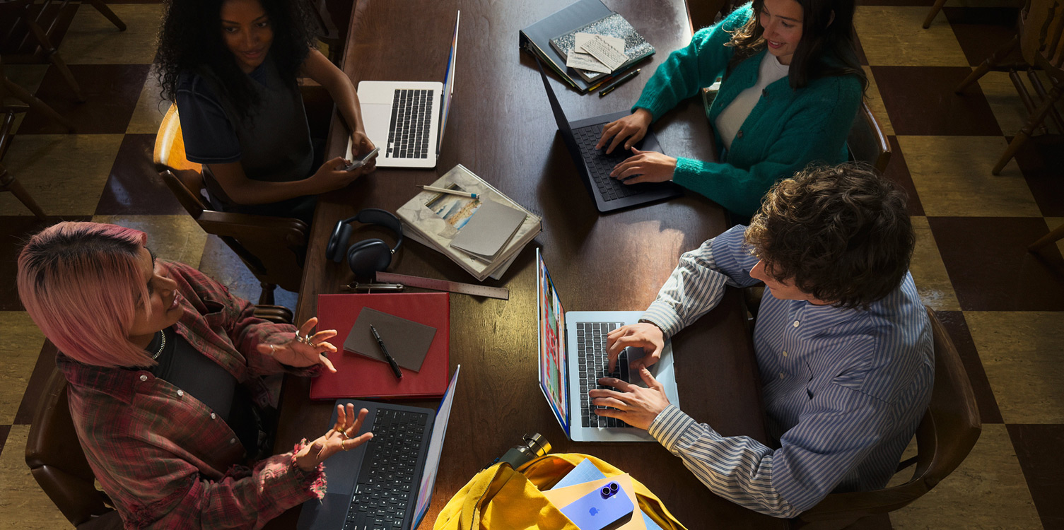 Vier studenten zitten aan tafel. Ze hebben hun MacBooks en aantekeningen open voor zich.