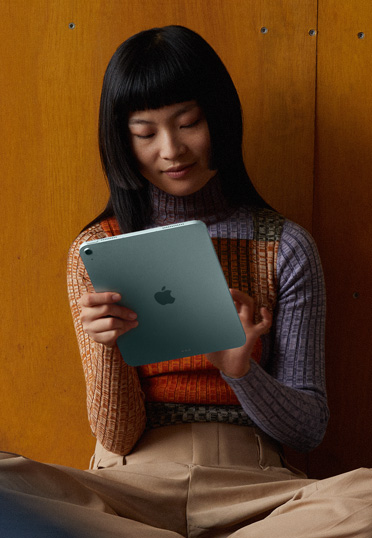 Een studente zit op de grond tegen een muur. Ze heeft een iPad vast.