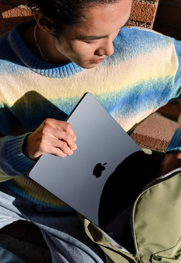 Een student die buiten zit. Hij haalt een gesloten MacBook uit zijn rugzak.