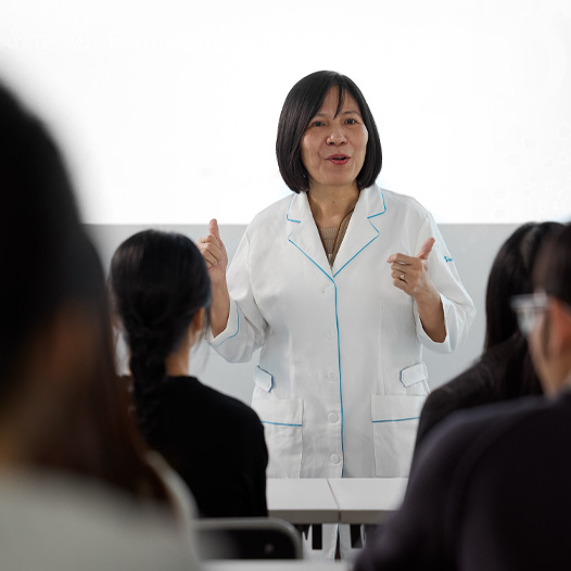 一名身穿白色實驗室外套的講師在坐滿學生的教室前面授課