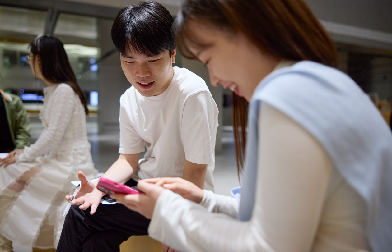 兩個人邊交談邊低頭看著 iPhone，其中一人拿著 iPhone 在瀏覽