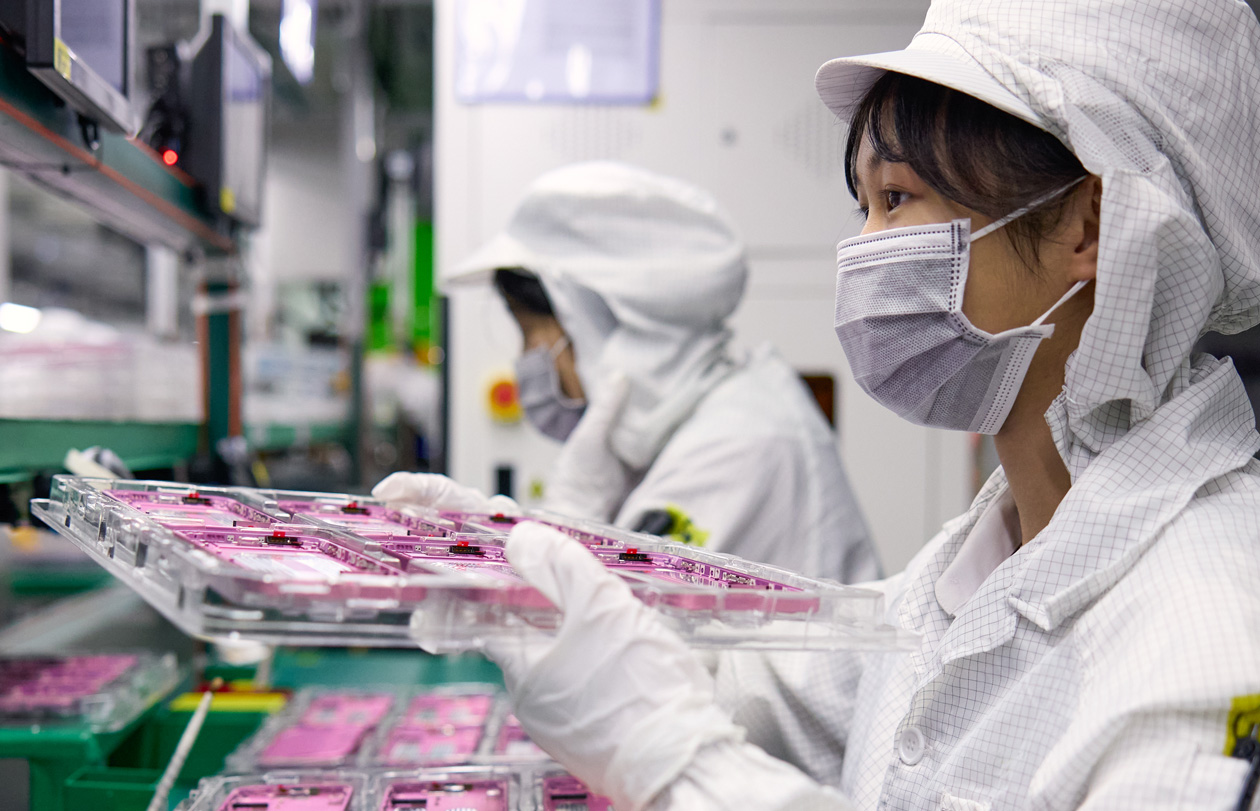 兩名身穿全罩工作服的員工在組裝廠區處理 iPhone 零組件