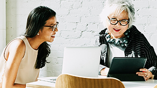 Two women looking at computer screens and smiling.