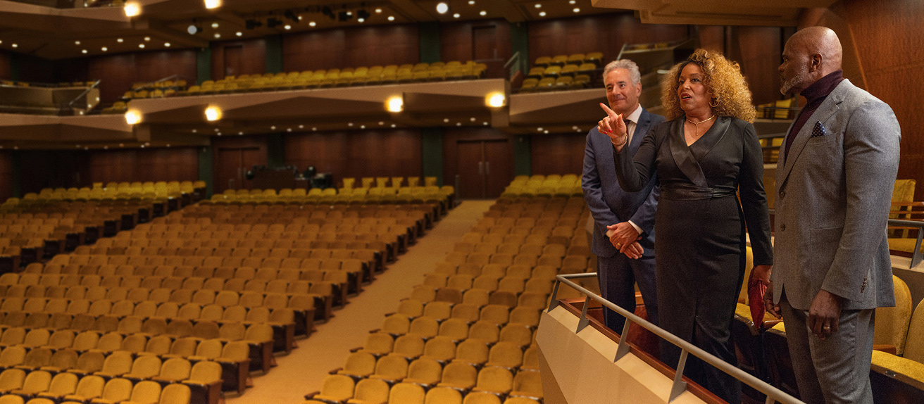 A group of people standing on a balcony in an empty theatre.
